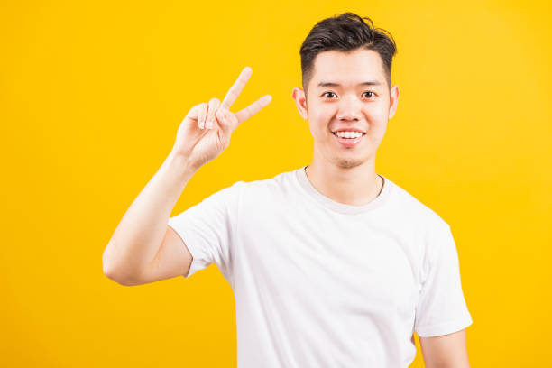istock young man smiling standing he showing fingers doing victory V sign 1328073246