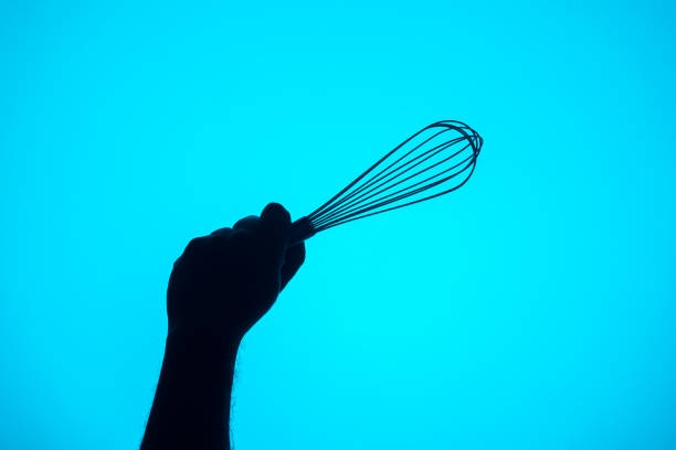 istock Stainless steel hand whisk held with one hand on a blue background 1328076719