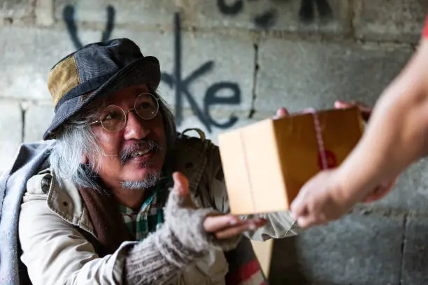 Photo of Homeless man receiving gift box from people hands at abandoned building or on street in the city