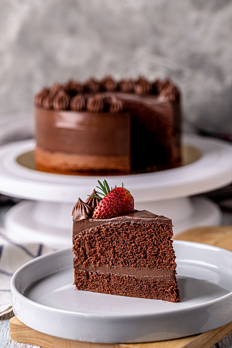 Slice of delicious homemade chocolate cake soft fudge topping with strawberry on white plate.