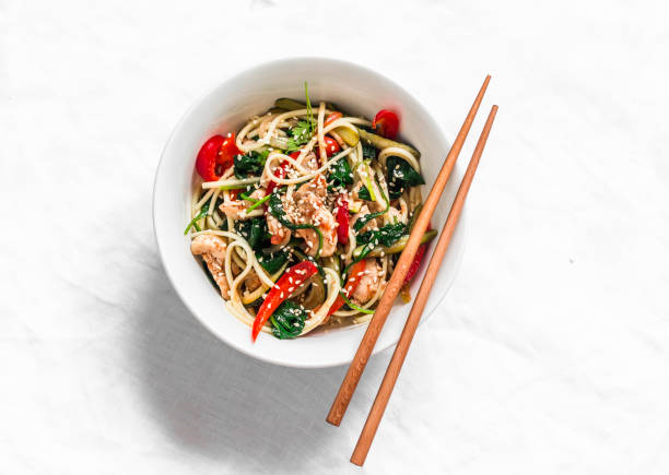 Stir fry vegetables zucchini, pepper, spinach and chicken with egg noodles on a light background, top view