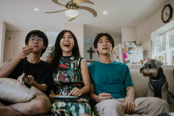 기쁨 아시아 가족과 귀여운 개는 거실에서 소파에 앉아 행복하고 주말에 tv 카벨 채널에서 만화를 보는 동안 함께 큰 소리로 웃음 - 스톡 사진 - humor men laughing teenager 뉴스 사진 이미지
