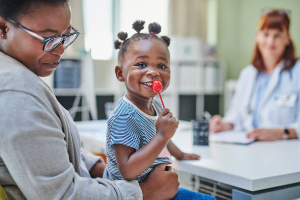shot of an adorable little girl getting a lollipop from her doctor during a checkup with her mother - family child portrait little girls imagens e fotografias de stock