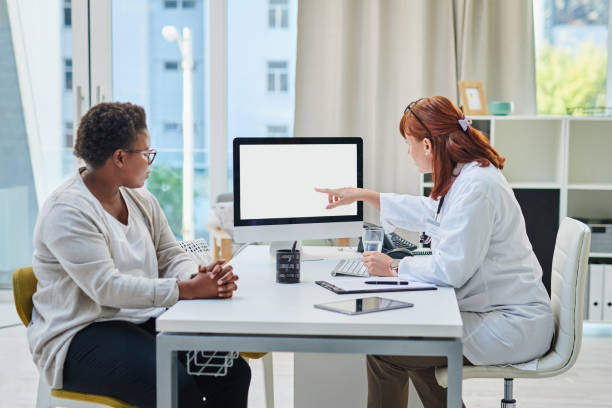 Shot of a doctor using a computer during a consultation with a woman stock photo