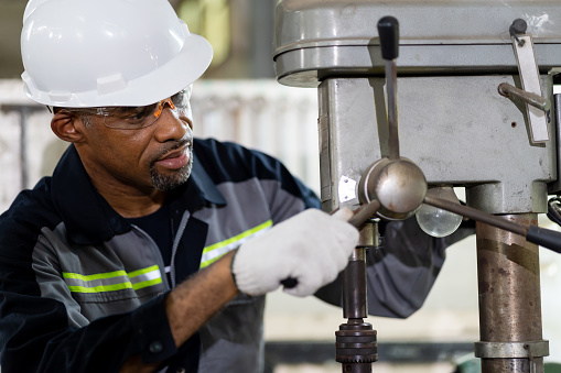 African American male engineer worker maintenance lathe machine in the factory. Black male worker working with machine with safety uniform, goggles and helmet