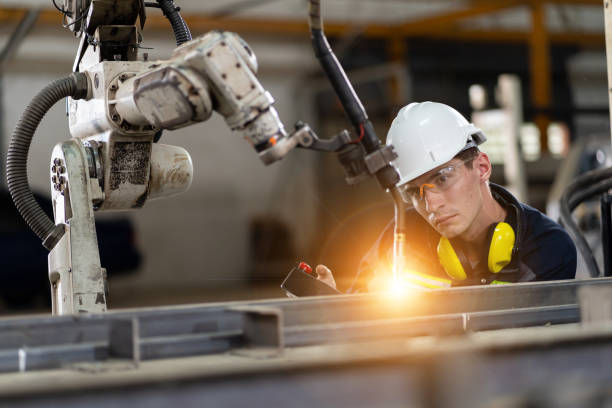 Male engineer holding robot controller for maintenance or repair automatic robotic machine in factory. Male technician worker working with control automatic robot arm system welding in the factory ingeniero masculino que sostiene el controlador del robot para el mantenimiento o la reparación de la máquina robótica automática en la fábrica. trabajador técnico masculino que trabaja con el sistema de brazo robot automático de control de soldadur