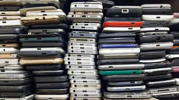 Photo of Background of damaged mobile phones. A bunch of broken smartphones. Used phones stacked on top of each other. Repair services and maintenance of equipment.