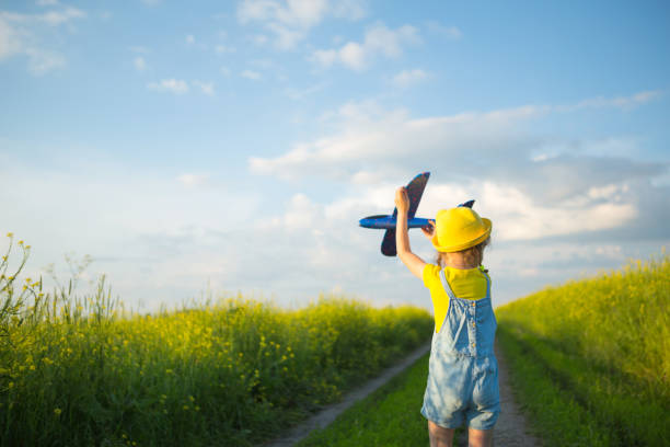 une fille au chapeau jaune lance un avion-mouche dans le champ, regarde le sentier. heure d’été, enfance, rêves et insouciance. visite en avion d’une agence de voyages lors d’un voyage, d’une aventure et de vacances. - jet fighter plane air vehicle airplane photos et images de collection