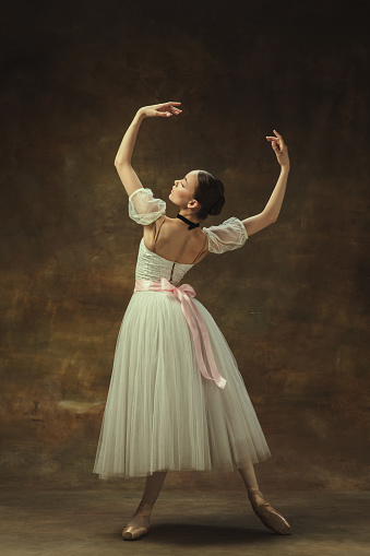 Elegance. Pretty young woman,, graceful female ballet dance in white ballet dress posing isolated on dark studio background. Art, motion, action, inspiration concept.. Smoothness of lines