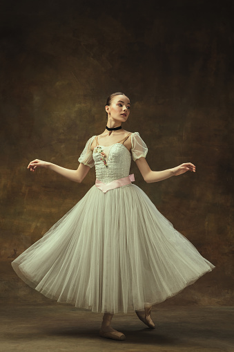 Feelings, emotions in classic ballet.. Beautiful girl, graceful female ballet dance in white ballet dress posing isolated on dark studio background. Art, motion, action, inspiration concept.. Smoothness of lines