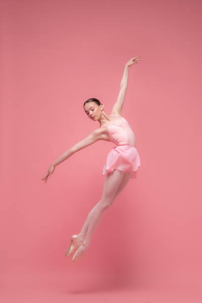 Young classical ballet dancer girl in dance class. Beautiful graceful ballerina practice ballet positions in pink tutu skirt in white light hall