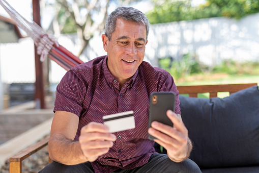 Mature Man Paying Bills or Online Shopping with a Credit Card in his Backyard