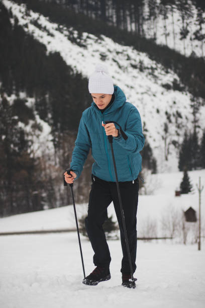 istock teenager in a white cap with a pompom and a blue jacket climbs a mountain using trekking poles for better stability and easier ascent. Fitness change. Walk in the mountains 1328107731