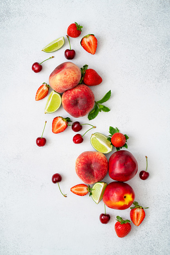 Peach, cherry, strawberry, lime, mint and nectarine on grey textured background. Fresh juicy fruits and berries. Healthy paleo diet food. Superfood nutrition concept. Summer snack. Top view, flat lay.