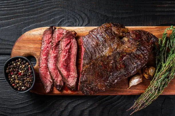 Grilled Butchers choice steak Onglet Hanging Tender beef meat on a cutting board. Black wooden background. Top View.