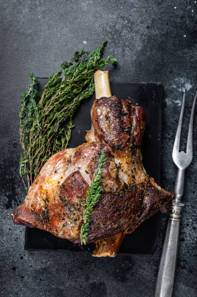 istock Oven Roasted lamb mutton whole leg with thyme. Black background. Top view 1328125981