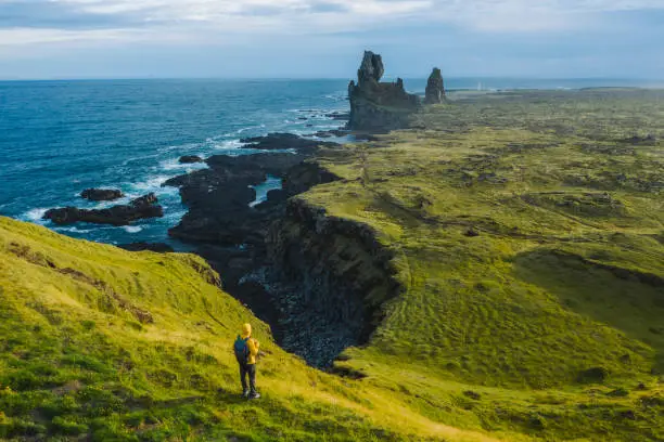 Photo of Man hiker in yellow jacket stand on the peak of the rock in outdoor park in Iceland. Londrangar