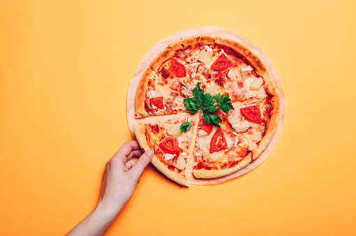 Woman hand taking one pizza slice, on an orange seamless background. Delicious Italian food.