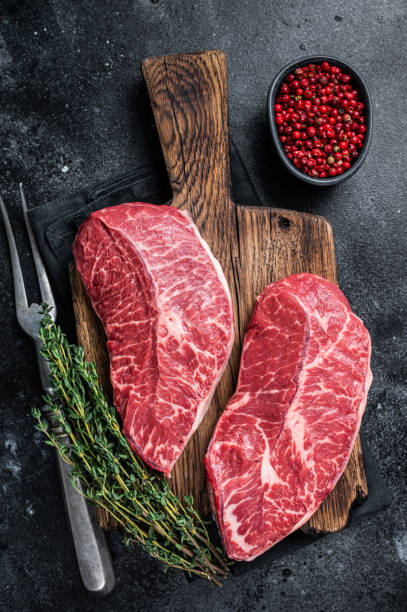 istock Fresh Raw Top Blade or flat iron beef meat steaks on a butcher cutting board. Black background. Top View 1328129128