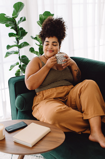 Attractive woman smiling with coffee mug. Pretty female smiling and holding coffee cup while sitting on couch at home.