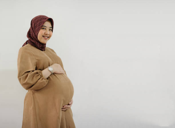 Muslim woman holding her pregnant belly and smiling stock photo