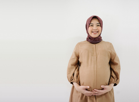 pregnant asian muslim woman holding her belly and smiling