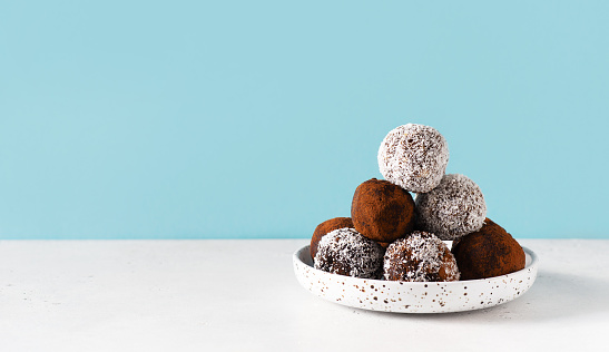 Carob energy balls with nuts, dates and coconut, vegan and vegetarian sweet food, blue background, copy space