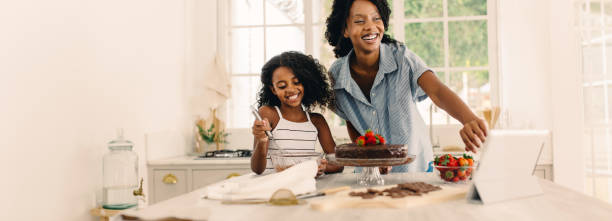 madre e hija divirtiéndose haciendo pastel con tableta digital - child digital tablet mother teaching fotografías e imágenes de stock