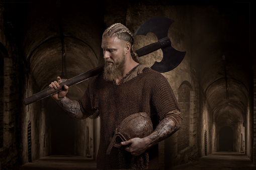 An armed handsome redhead viking warrior holding a sword in a fantasy outdoor fairytale setting