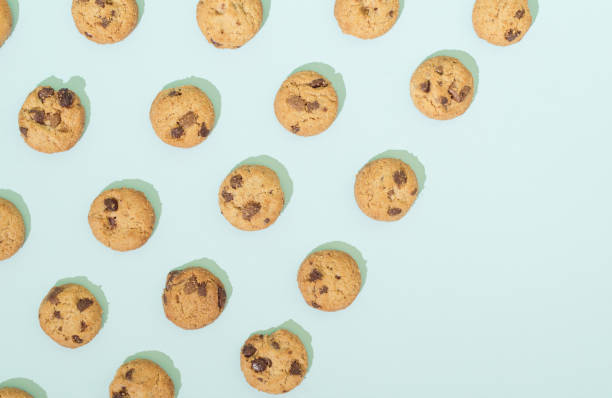 biscuits aux pépites de chocolat disposés selon un motif sur fond turquoise. concept de nourriture sucrée avec espace de copie. - coin chocolate food chocolate coin photos et images de collection