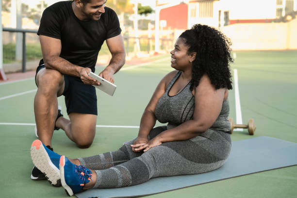Personal trainer working with curvy woman while giving her istruction with digital tablet during training session - Sport people lifestyle concept stock photo
