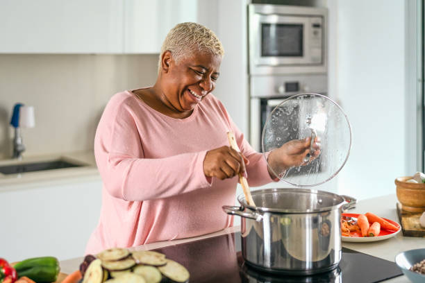 donna anziana felice che prepara il pranzo nella cucina moderna - madre ispanica che cucina per la famiglia a casa - stereotypical homemaker foto e immagini stock