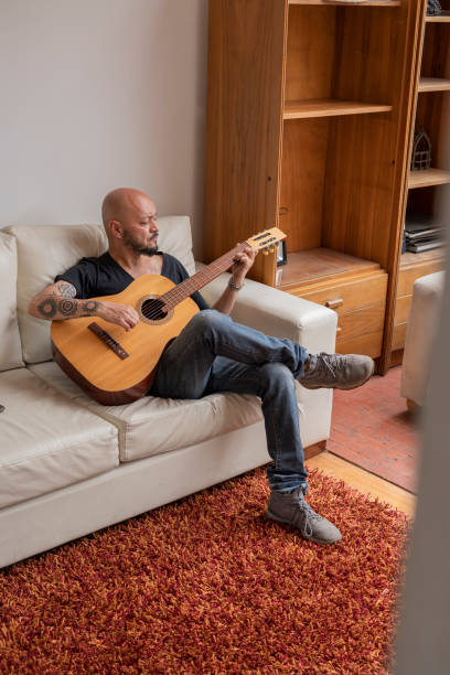 istock Man sitting on his sofa practicing the chords on his guitar while at home alone 1328144208