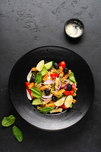 istock Whole grain pasta with vegetables on a white plate on black slate, stone or concrete background. Top view with copy space. 1328153927