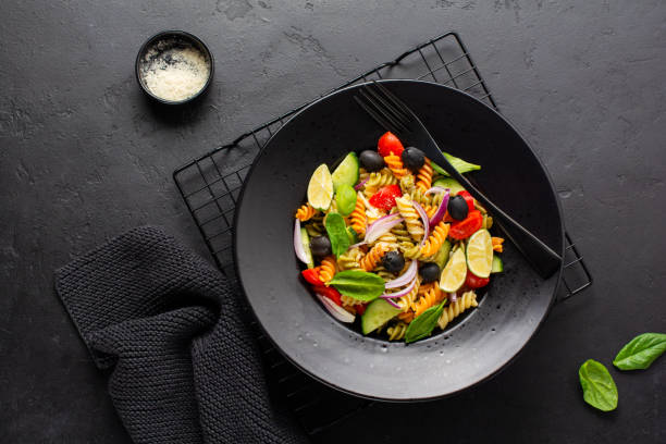istock Whole grain pasta with vegetables on a white plate on black slate, stone or concrete background. Top view with copy space. 1328154026