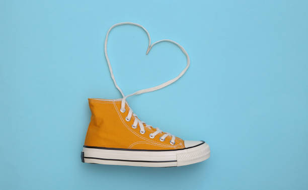 Yellow high-top sneaker (gumshoe) with untied heart shaped laces on blue background. Top view. Love concept Yellow high-top sneaker (gumshoe) with untied heart shaped laces on blue background. Top view. Love concept shoelace stock pictures, royalty-free photos & images