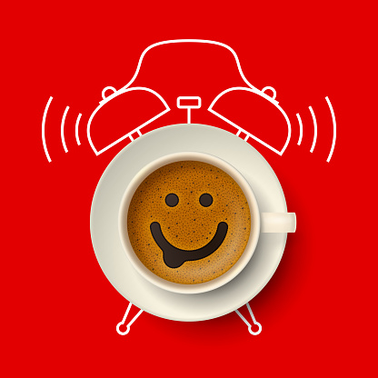 Cup of coffee with happy funny smiling face on frothy surface, on saucer, with silhouette of alarm clock on background. Time to have a coffee break, relax and cheer up, coffee time concept