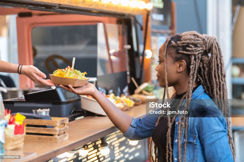 Satisfied afro american woman getting fast food tray with delicious nachos Afro american woman getting a delicious looking tray with nachos from a fast food truck. Selective focus: Fast food and lifestyle concept. Food Truck Stock Photo