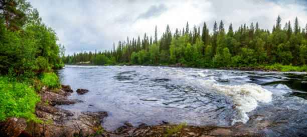 Panorama from the shore to the wide river expanses. Coniferous forest on one side. Deciduous forest on the other side. Red rocky shore. Rapids on the river. north. Karelia.