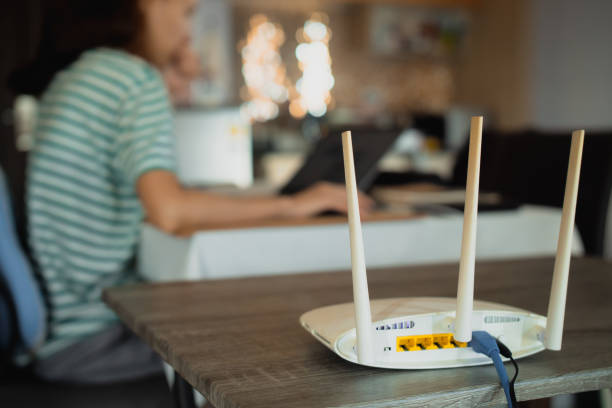 una mujer está trabajando en casa usando un módem router, conectando internet a su computadora portátil. - network connection plug cable computer cable telecommunications equipment fotografías e imágenes de stock