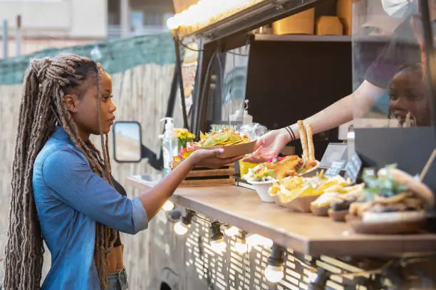 Photo of Calm afro american woman getting guacamole and nachos from a fast food truck: Selective focus