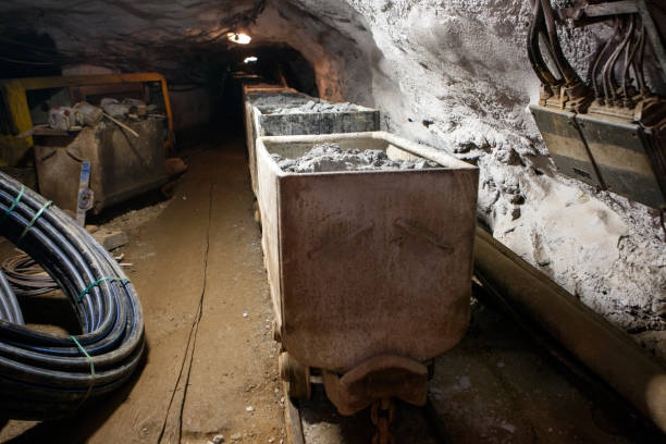 istock Hutch cart with raw material standing at underground mining. Production and technology concept. Tunnel with railway and electricity mine cables of underground mining. Transportation and lighting. 1328163322