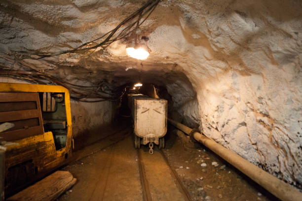 istock Hutch cart with raw material standing at underground mining. Production and technology concept. Tunnel with railway and electricity mine cables of underground mining. Transportation and lighting. 1328163324