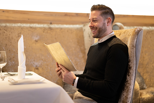 smiling man sitting at dinner table of luxury restaurant reading menu card