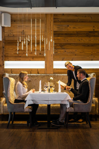 couple dining in luxury restaurant dinner for two in luxury restaurant of mountain hotel, with place for text, friendly female waiter showing menu card man chooseing  meal exclusive dinner stock pictures, royalty-free photos & images