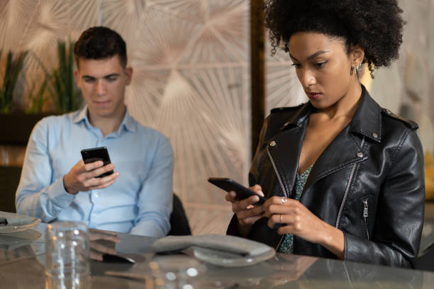 istock Young couple bored sitting at restaurant distracted by smartphone screen. People always connected to the internet addicted by technology concept. 1328176963