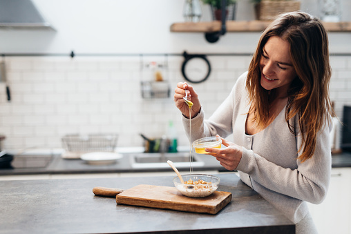 Young woman in the kitchen adds honey to muesli