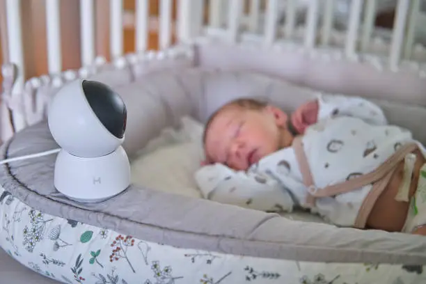 A surveillance camera Xiaomi Mi Home looks at the crib with a sleeping newborn baby - Moscow, Russia, June 27, 2021