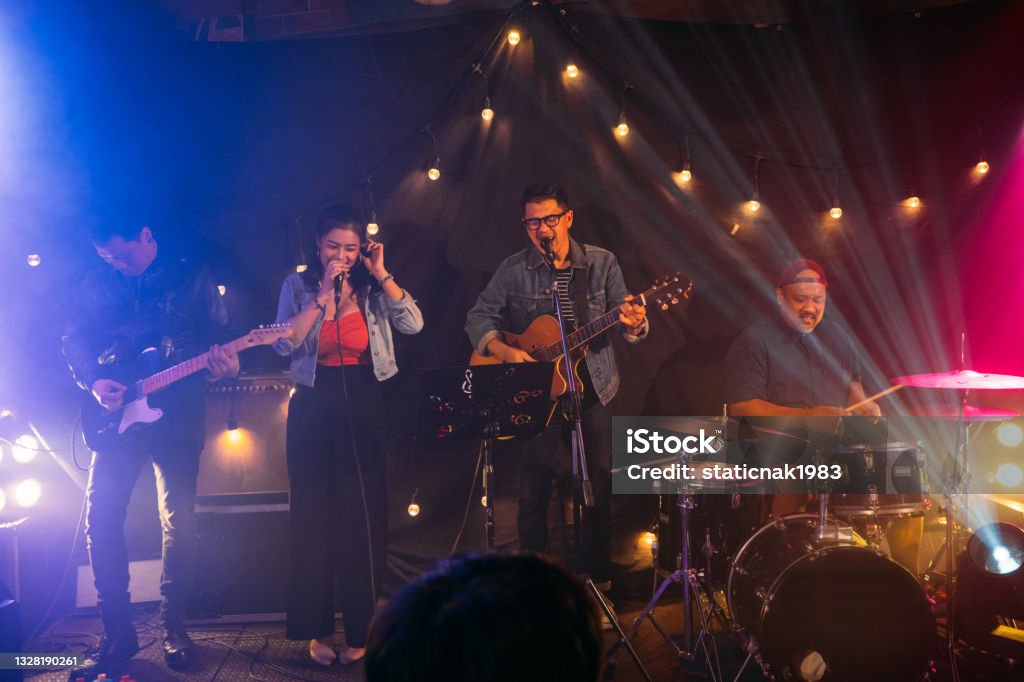 Musicians in concert. Males playing guitar or drum and female singing on a stage at night on weekend, Live music concept. Performance Group Stock Photo