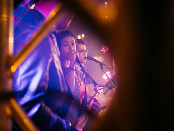 Professional Rock Musicians Performing Under Falling Confetti on Festival Stage, Playing Popular Rock Tracks in Front of a Crowded Concert Arena. Electrifying Performance at an Indoors Festival